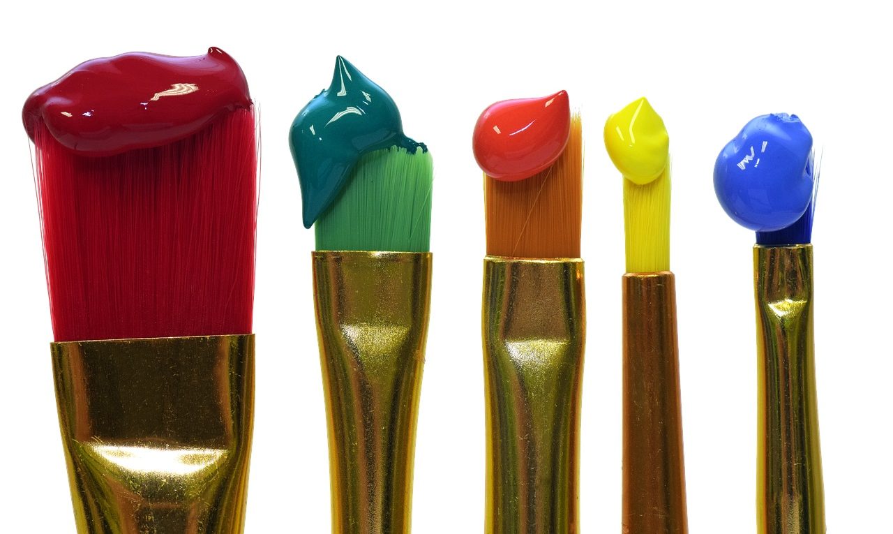 Cinq pinceaux chargés de peinture de couleurs différentes